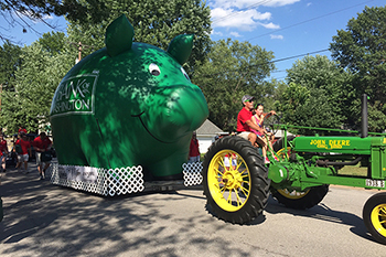 Bank of Washington employee driving tractor pulling big, inflatable pig in parade