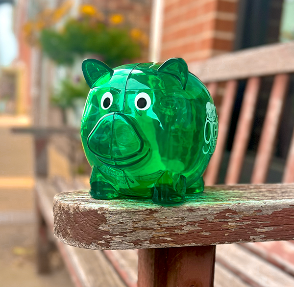 green piggy bank on a bench on a downtown sidewalk