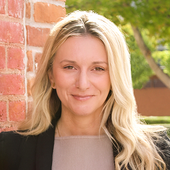 Upclose photo of Bank of Washington employee Alja Zigic leaning on brick wall smiling with green tree in the background