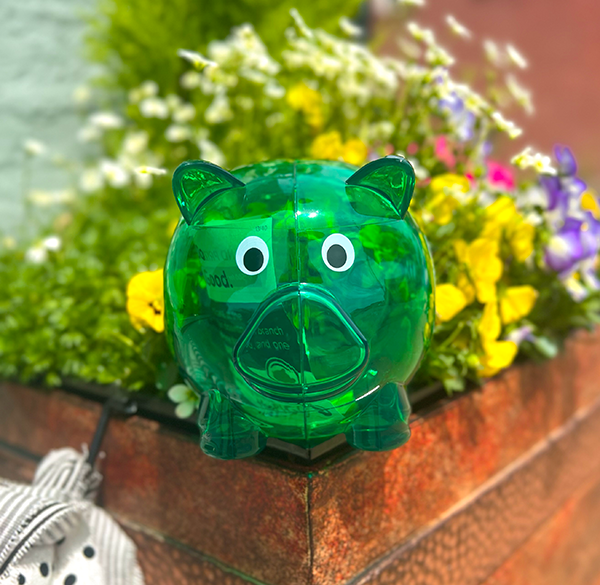 green piggy bank hidden in a flower pot full of yellow, white, and purple flowers