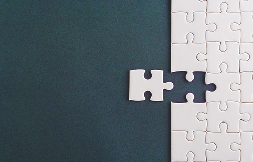 white puzzle piece fitting into large puzzle on gray background