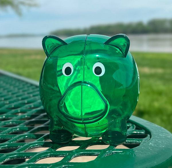 green piggy bank on a bench at a riverfront park during a sunny day