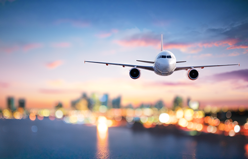white plane flying in front of blurred colorful background of city